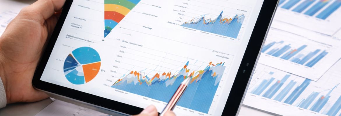 Pessoa a segurar um tablet onde estão apresentados vários gráficos e visualizações de dados, incluindo gráficos de linhas, de barras e um gráfico circular. Ao lado, encontram-se folhas impressas com gráficos semelhantes, sugerindo análise ou monitorização de desempenho estatístico ou financeiro.